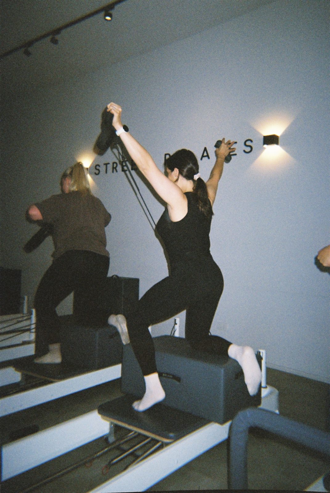 A Street member pressing overhead on the reformer, Street Pilates signage on the wall